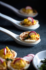 Deviled eggs garnished with smoked paprika , sliced radish , and chopped basil.
