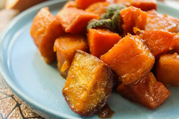appetizing sliced baked sweet potato in sweet and sour sauce on a blue plate selective focus,...