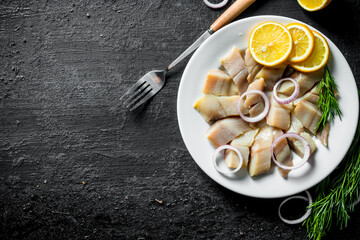 Pieces of salted herring on a plate with sliced lemon and onion.