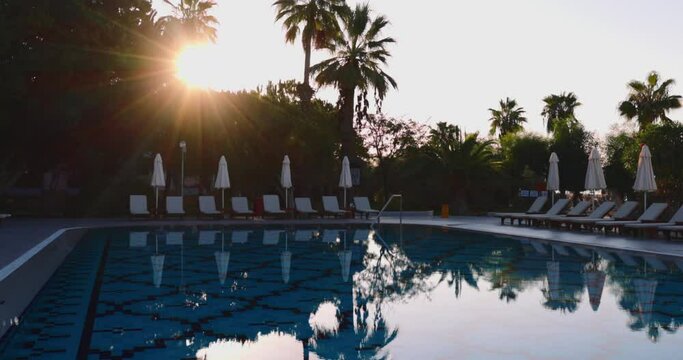 Luxury resort pool scene with empty deck chairs and folded parasols, ready for guests to relax and soak up the sun.