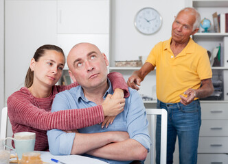 Fototapeta premium Unhappy family couple hugging after conflict, worried elderly man on backgroud
