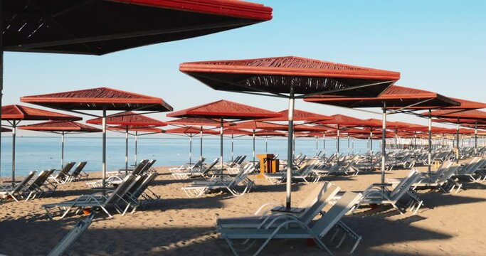 Empty deck chairs and wooden sunshades arranged in a row on sandy beach at seaside with clear blue sky in the background during sunny day