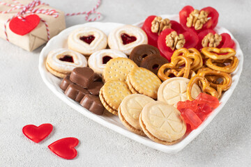 Heart shaped plate with shortbread, chocolate hearts, red candies and nuts for Valentine's Day on gray background