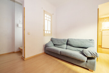 Living room of a house with a solitary two-seater sofa upholstered in blue fabric and a white...