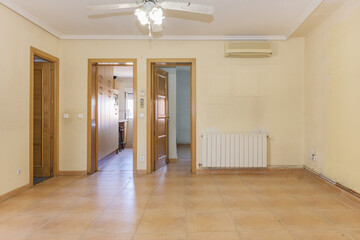 Living room of an empty house with oak wooden doors with light brown tile floors and a fourteen segment aluminum radiator