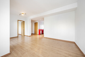 Empty living room with oak flooring and door carpentry and skirting boards of the same material and an open kitchen in the background