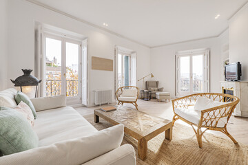 Living room of a house with multiple balconies facing the street with white wooden shutters and wicker furniture and jute fiber rugs