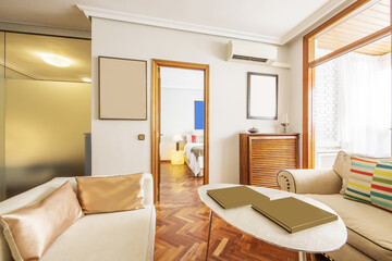 Living room of a house with white fabric armchairs, jatoba parquet floors, wooden radiator covers and access to other rooms