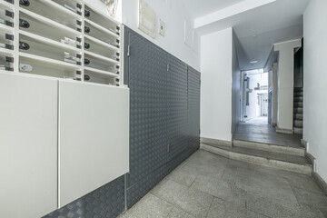 Access portal to a building with granite tiles on the stairs to access an elevator with gray doors and wrought iron railing and methacrylate letterboxes