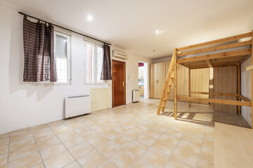 Open loft-style apartment with a living room with light brown square stoneware floors and white aluminum windows with curtains and a raised wooden bed frame