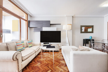Apartment with a living room furnished with white sofas of various styles and a TV in a bookcase