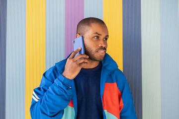 Young African-American woman talks on a mobile phone dressed casually in blue sportswear. The black man relates by talking socially through technology on a colorful grated background on the street.