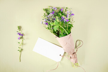 Cute bouquet of Germander Speedwell (Veronica chamaedrys) flowers wildflowers is packed in craft paper, tied with twine, with a blank card on a light yellow background