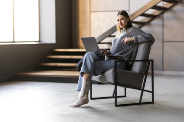 Happy woman holding laptop while sitting on a chair over gray background