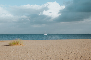 Fototapeta na wymiar Horizontal view of a sailing boat in front of a beach with a blue sky in Amager beach, Copenhagen