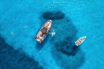Aerial view of yachts and swimming people in blue sea at sunset in summer. Sardinia, Italy. View from above of speed boats, yachts, transparent water. Top view from drone. Tropical seascape. Vacation - obrazy, fototapety, plakaty