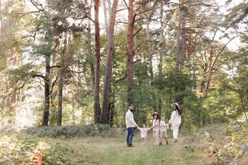 Back view of mother, father with three kids are walking, having fun in autumn forest. Family holding children hands enjoying time together at nature background. Happy parenthood and childhood concept