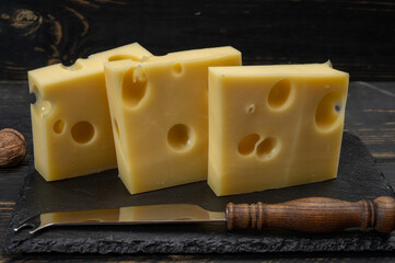 Block of Swiss medium-hard yellow cheese emmental or emmentaler with round holes and cheese knife