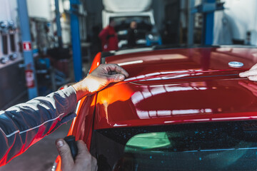 Mechanic customizes car removing spoiler using cutting cord in an auto repair shop. High-quality...
