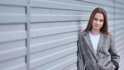 Portrait of a young girl in a blazer by a wall on the street.