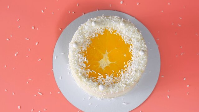 Cake with orange and coconut shavings spun on a pink background.