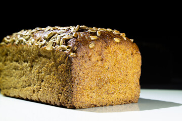 rye bread in the shape of a parallelepiped sprinkled with sunflower seeds on a white table and with a blurred background on a black background