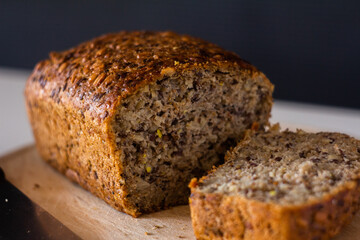 bread with different seeds sliced on a wooden cutting board on a white table with a dark background