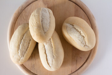 wheat buns for baking on a round wooden cutting board on a white background top view