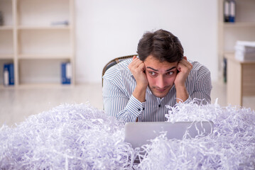 Young male employee and a lot of cut papers in the office