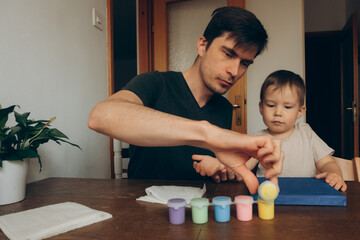 Fototapeta premium dad and son are painting on canvas at the table with brushes with multicolored paints