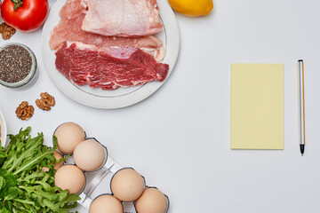 food that includes meat, eggs, tomatoes, and other ingredients on a white table with an open notebook next to it
