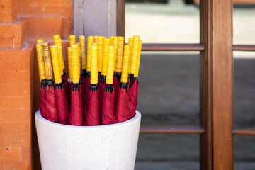 A red umbrella with a yellow handle is placed in a ceramic pot outdoors.