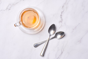 two spoons and a cup of tea on a marble table with a silver spoon in the bowl is next to it