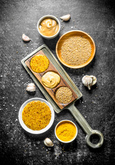 Different types of mustard in plates and on a stand with garlic slices.