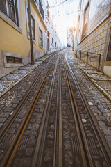 Obraz premium A vertical wide-angle view of a tramway lane over the Portuguese paving stone on a narrow picturesque Lisbon neighborhood in shades of yellow on the walls of the surrounding residential buildings