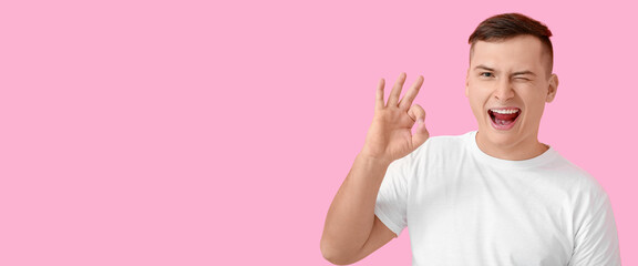 Happy young man showing OK on pink background with space for text
