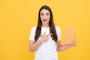 Funny surprised teen girl with notebooks standing over yellow background with copy space. Educational concept for school. Portrait of young student.