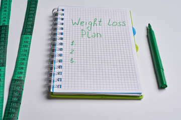 an open notebook with a green pen next to it and a measuring tape on the side. Weight loss plan
