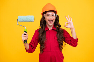 Excited teenager girl. Painter in workshop. Renovation and repair. Teen girl in helmet with painting brush. Child in hard hat. Kid builder painter on construction site.