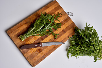 some greens on a cutting board next to a knife and a piece of lete with it's end cut in half