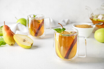 Glass cup of fruit tea with pear, mint and cinnamon on light background, closeup