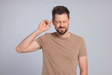 Fototapeta premium Man cleaning ears and suffering from pain on grey background