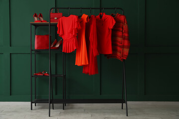 Rack with red clothes, shelving unit and shoes near green wall