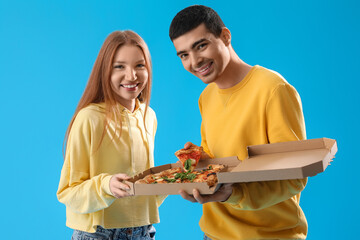 Young couple with box of tasty pizza on blue background