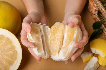 Female hands with halves of sweet pomelo fruits on beige background, closeup