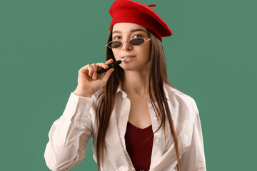 Stylish young woman with disposable electronic cigarette on green background, closeup