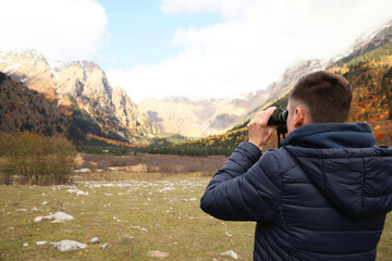 Boy looking through binoculars in beautiful mountains, back view. Space for text