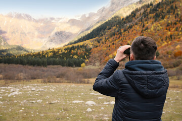 Fototapeta na wymiar Boy looking through binoculars in beautiful mountains, back view. Space for text