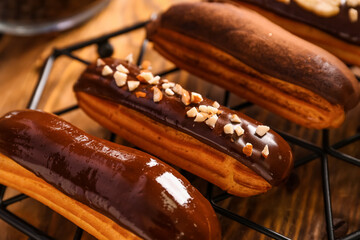 Grid with tasty chocolate eclairs on wooden background, closeup