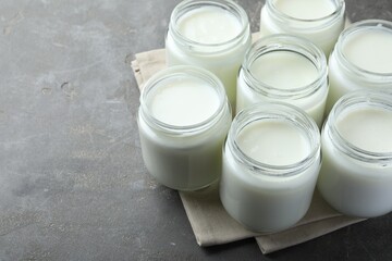 Tasty yogurt in glass jars on grey table. Space for text
